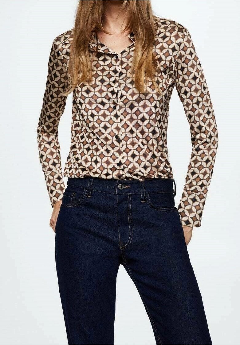 Femme portant une chemise boutonnée à manches longues avec un motif géométrique marron et beige et un jean taille haute bleu foncé.