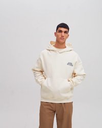 Sweatshirt couleur crème en tissu doux, doté d'une poche avant et d'une broderie "APER STUDIOS" sur la partie gauche de la poitrine.