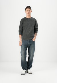 Dark gray knitted sweater with a crew neckline, paired with light blue straight-leg jeans and white sneakers with black accents.