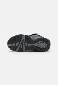 Suela de zapato deportivo negro con un patrón de tracción robusto, que presenta una superficie de goma texturizada y surcos prominentes para ofrecer agarre.