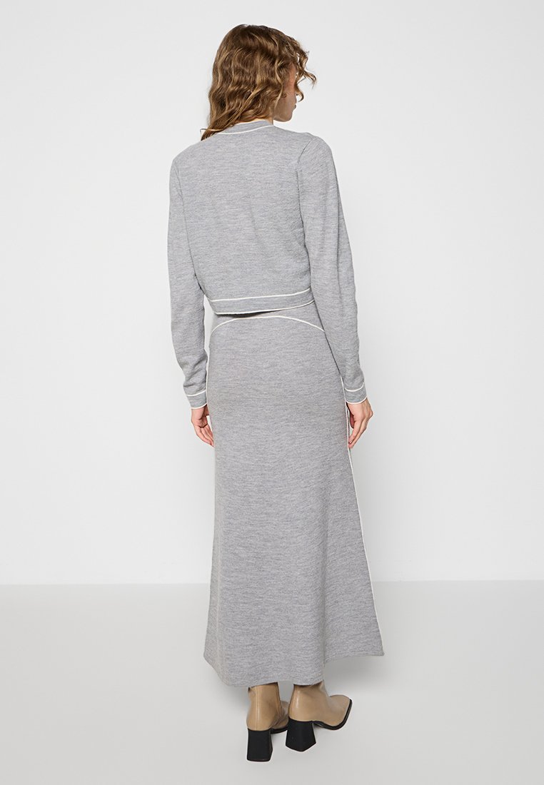 Graues, gestricktes Zweiteiler-Outfit bestehend aus einem Crop-Top und einem Maxi-Rock, mit kontrastierenden weißen Blenden und einer glatten Textur. Getragen mit beigen Knöchelstiefeln.