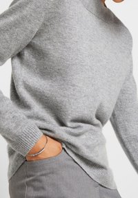 Hellgrauer Strickpullover mit Rundhalsausschnitt, gerippten Bündchen, Seitenschlitzen und weicher Textur, kombiniert mit maßgeschneiderten grauen Hosen.