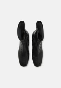 Bottines noires en cuir avec une texture lisse, dotées d'une fermeture éclair latérale et d'un bout légèrement arrondi. Intérieur doublé pour plus de confort.