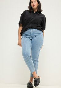 Camisa negra de botones, jeans de rayas azul claro y zapatos negros sin cordones con un acento de cadena. Diseño de atuendo simple y casual.