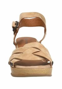 Beige suède sandaal met een breed bandontwerp, verstelbare enkelriem en een houten plateauzool. Bevat decoratieve uitsparingen en donkere accenten.