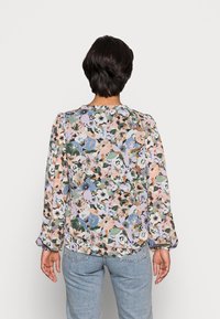 Blouse florale avec un motif multicolore de fleurs roses, bleues et vertes ; tissu léger avec des manches bouffantes et un col rond.