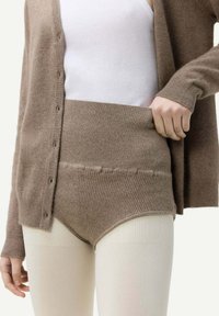 Brun stickad cardigan över en vit tanktop, parat med högmidjade beige stickade shorts. Mjuk textur och ribbad detalj syns.