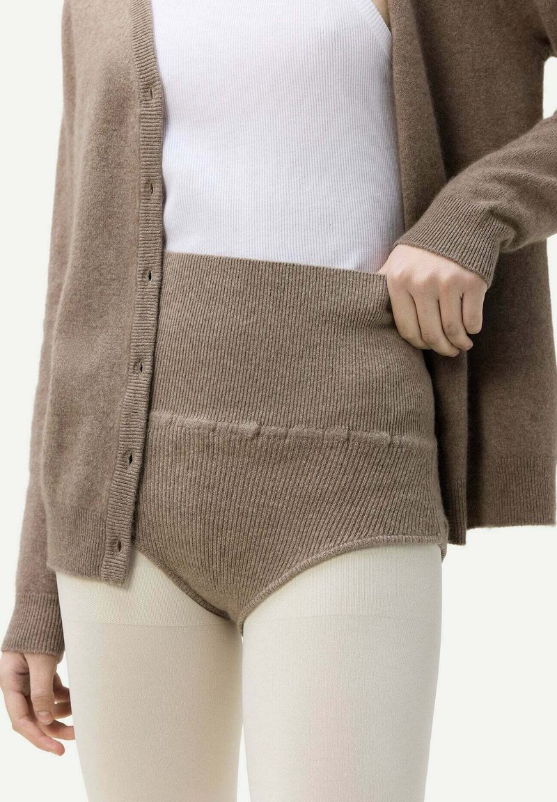 Brun stickad cardigan över en vit tanktop, parat med högmidjade beige stickade shorts. Mjuk textur och ribbad detalj syns.