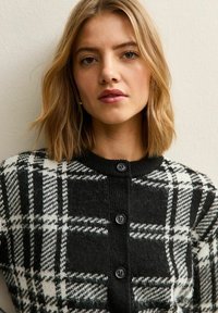 Czarny i biały kardigan w kratę z guzikami z przodu, prążkowanym kołnierzem i miękkim, teksturowanym materiałem, umieszczony na neutralnym tle.