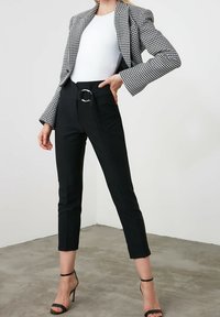 Svarta skräddarsydda byxor med en cirkulär spänne fram, kombinerat med en vit topp och en rutad kavaj. Outfiten har strukturerade axlar och smalnande ben.