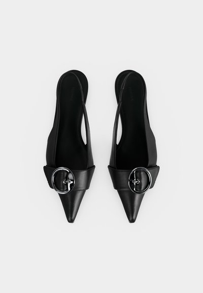 Ζευγάρι μαύρα γόβες με μύτη μυτερή και λουράκι στον αστράγαλο με πλατιά λωρίδα και μεγάλο ασημένιο αγκράφα, εμφανίζεται σε λευκό φόντο.