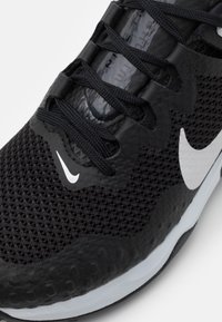 Musta urheilukengä, jossa on verkkosukkia, teksturoituja yksityiskohtia, valkoinen Nike-logo ja mustat nauhat. Pohja on osittain valkoinen ja siinä on kuvioitunut pito.