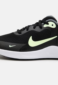 Baskets de sport noires avec empeigne en mesh, logo Nike jaune-vert notable, accents gris et semelle blanche, présentant un design texturé pour une meilleure adhérence.