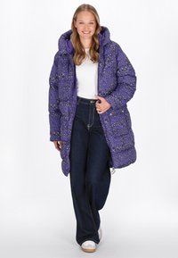 Lila Puffermantel mit Kapuze, ausgestattet mit einem schwarz-grünen Leopardenmuster, mit Reißverschluss und Seiten Taschen, kombiniert mit dunklen Jeans.