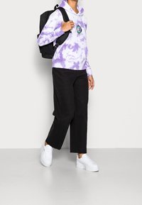 Purple tie-dye hoodie with logo, black wide-leg pants, and white platform sneakers. The outfit features a relaxed fit and casual style.