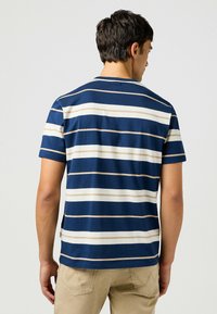 Camiseta de manga corta a rayas en azul marino y crema, con cuello redondo, fabricada en tejido suave y con una etiqueta colocada en la parte posterior.