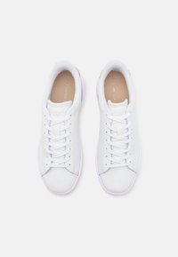 Baskets en cuir blanc avec une texture lisse, dotées de lacets blancs et d'une semelle en caoutchouc légère de couleur violet pâle. Design minimaliste avec une semelle intérieure signée.