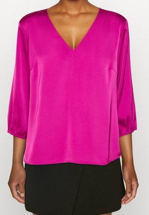 Blouse en satin fuchsia avec un col en V, des manches trois-quarts et des poignets élastiqués, associée à une jupe noire. Texture lisse et tombé fluide.