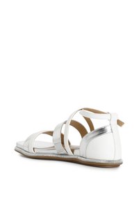 Sandales blanches avec des accents argentés, design ouvert, semelle plate, comprenant plusieurs straps sur le dessus et un bord pailleté.