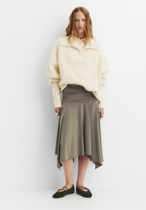 Crème, oversized gebreide trui met kraag, gecombineerd met een gedrapeerde, olijfgroene midi rok en donkerbruine flats. Soepele textuur, relaxte pasvorm.
