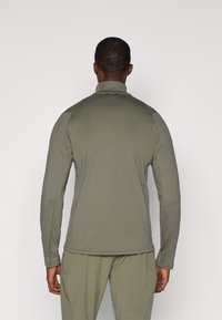 Herren Langarmoberteil in Olivgrün, aus strukturiertem Stoff gefertigt, hat einen hohen Kragen und eine figurbetonte Silhouette. Minimale Markenkennzeichnung sichtbar.