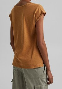 T-shirt à manches courtes de couleur moutarde avec un col rond et des manches retroussées. Texture douce, coupe décontractée, vue de dos montrée.