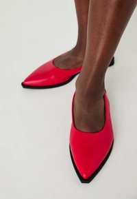 Ballerine rosse in pelle con punta appuntita e tacco basso in robusta finitura nera. Texture liscia e design minimalista, con un'apertura ampia e una silhouette angolare.