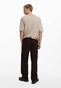 Beige oversized t-shirt parret med brune cargo bukser; har sidelommer, en løs pasform og struktureret stof. Brune fodtøj fuldender looket.