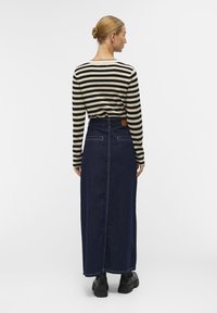 Haut à manches longues rayé noir et beige associé à une jupe maxi en denim bleu foncé, dotée d'une fente arrière et de poches en patch. Chaussures noires.