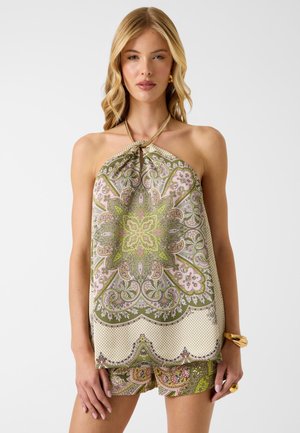 Femme portant un top dos-nu à motifs et un short assorti avec des motifs cachemire verts, roses et beiges, accessoirisée de bijoux en or.