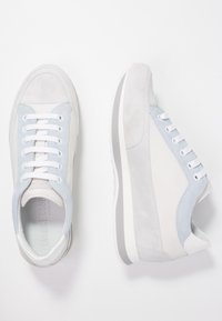 Grå och vita sneakers i mocka och läder, med ljusblå detaljer, platta vita snören och en texturerad sula.