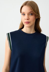 Marineblauw mouwloos topje met een ronde halslijn, voorzien van contrasterende groen-witte gestreepte accenten op de schouders, gemaakt van een zachte stof.