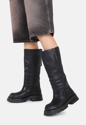 Black leather knee-high boots featuring a pleated design, round toe, durable sole, and ankle strap with a buckle detail.