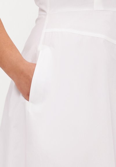Robe blanche avec une poche latérale et une texture lisse et nette. Le design présente des lignes épurées et des détails de couture subtils.