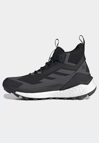 Chaussure de sport montante noire avec tige en mesh, lacets noirs, semelle épaisse blanche amortissante et languettes à tirer sur la languette et le talon.