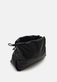Pochette en cuir noir souple avec une fermeture à cordon sur fond clair, inclinée pour montrer sa forme souple.