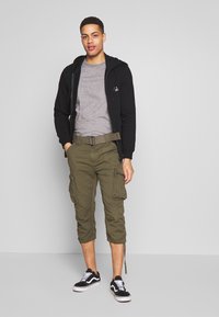 Schwarze Reißverschluss-Hoodie, graues T-Shirt, olivfarbene Cargo-Hosen mit Seitentaschen und schwarze Sneakers mit weißen Sohlen. Lässiges Outfit.