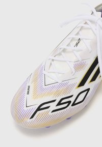 White soccer cleat with black and gold accents, featuring a textured surface and gradient pattern. Laces are white, and the model number is 'F50.'