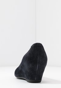 Scarpa con zeppa in suede nero caratterizzata da un design affusolato, una texture liscia e un retro curvo, adatta per occasioni formali o informali.