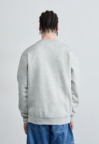 Sudadera gris con cuello redondo, mangas largas, puños y dobladillo acanalados, hecha de un suave material de algodón, con una textura lisa.