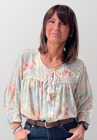 Blusa floreale azzurra con vita arricciata, caratterizzata da motivi di fiori rosa e verdi, dettaglio con fiocco anteriore e maniche ampie e leggere.