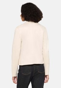 Crèmekleurig neplederen jack met een getailleerd ontwerp, ronde kraag en nette stikdetails; gecombineerd met donkere denim jeans.