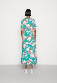 Vestido maxi floral com fundo turquesa, apresentando flores em rosa e branco, mangas curtas e um corte solto, combinado com ténis brancos.