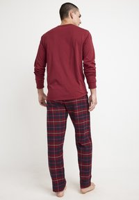 Red long-sleeve cotton top paired with plaid pajama pants featuring blue and white lines on a red background, designed for comfort.
