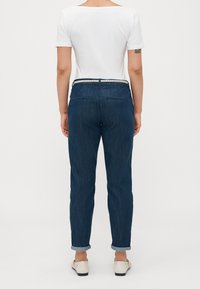 Tmavě modré džíny s ohrnutými nohavicemi, tkaným páskem a zadními kapsami. V kombinaci s jednoduchou bílou košilí s krátkým rukávem.