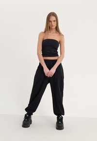 Top noir sans bretelles associé à un pantalon noir ample et des chaussures noires à semelle épaisse. Tissu lisse avec une taille élastique.
