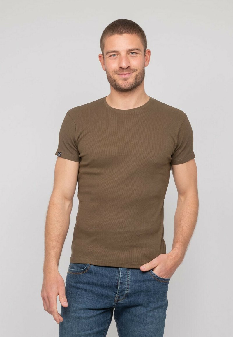 T-shirt vert olive à manches courtes et col rond, fabriqué en coton extensible, associé à un jean en denim bleu.