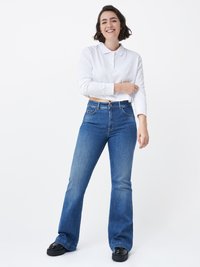 Polo shirt bianco leggero a maniche lunghe con colletto, abbinato a jeans a zampa d'elefante blu e scarpe con plateau nere. Design semplice e casual.