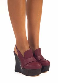Scarpe a zeppa bordeaux con una piattaforma nera texturizzata, dotate di una fascia larga e di un design elegante per un look moderno.