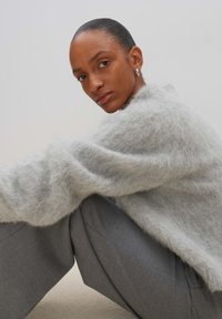 Hellgrauer, flauschiger Pullover mit lockerer Passform, kombiniert mit grauen, maßgeschneiderten Hosen. Texturiert und mit hohem Kragen. Schlichtes, unauffälliges Design.